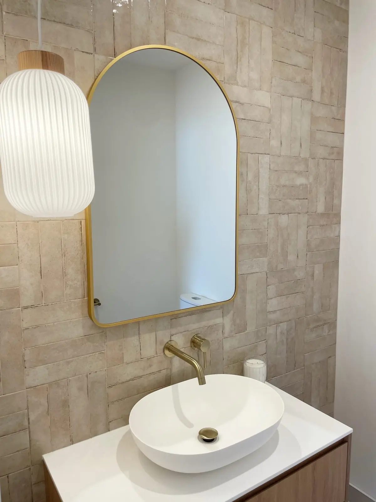 Bathroom vanity with a vessel basin, brushed brass tapware and an arched brass-framed mirror