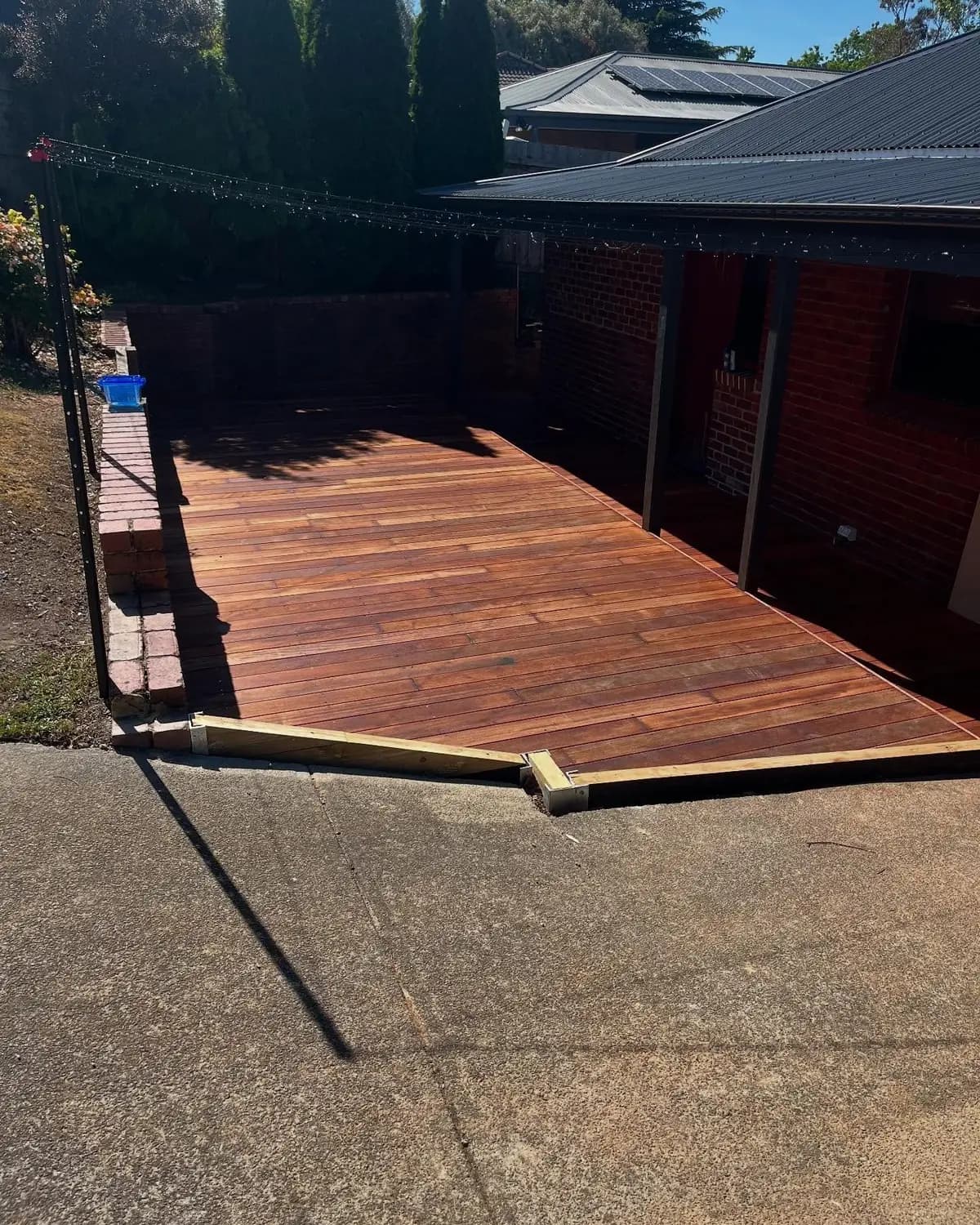 Finished hardwood backyard deck beside a red brick home