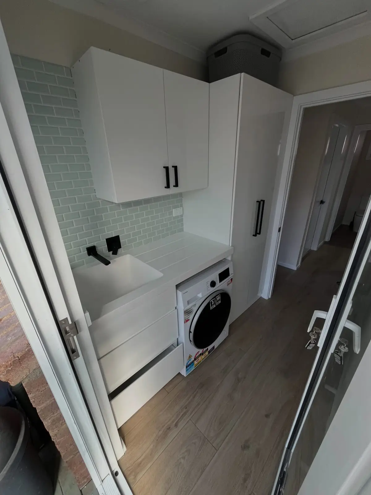 Renovated laundry with white cabinetry, a tiled splashback and a front-loading washer
