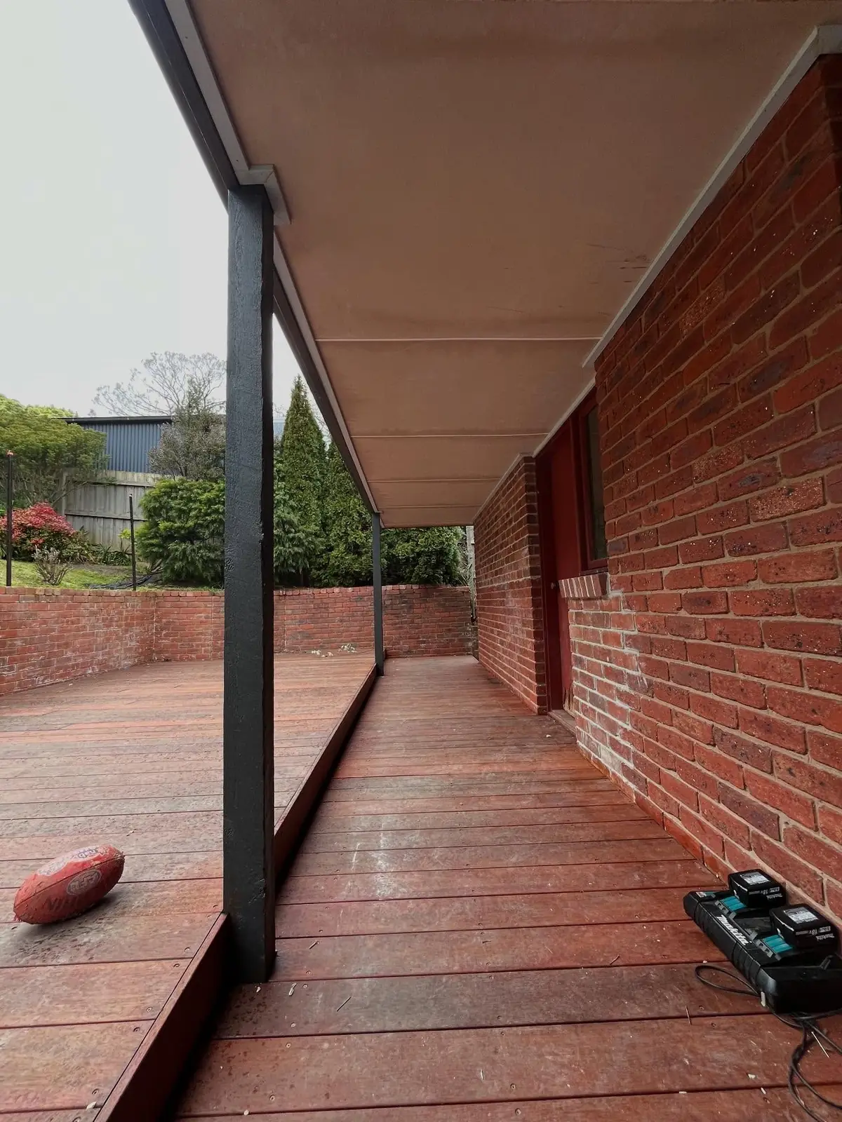 Hardwood verandah decking running along a red brick wall under a lined roof