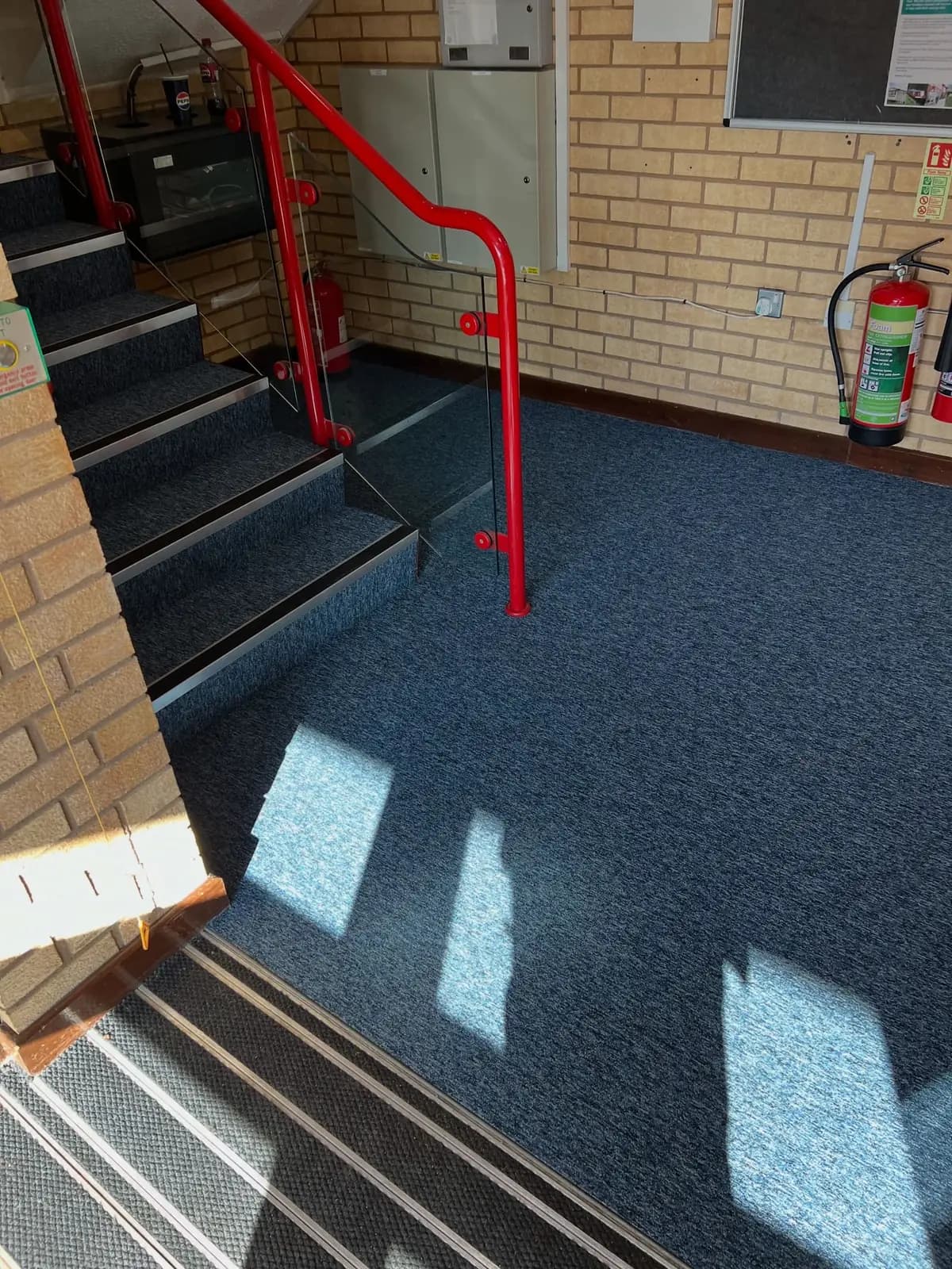 Communal stairwell landing with blue carpet tile, non-slip stair nosing and a red handrail