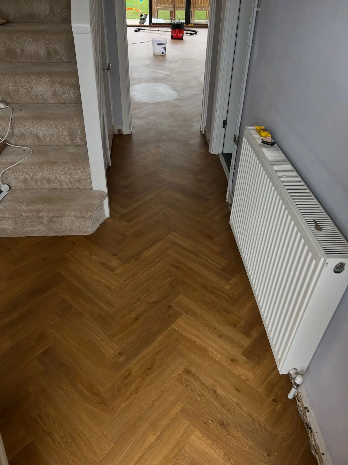 Herringbone oak-effect LVT running along a hallway past a carpeted staircase