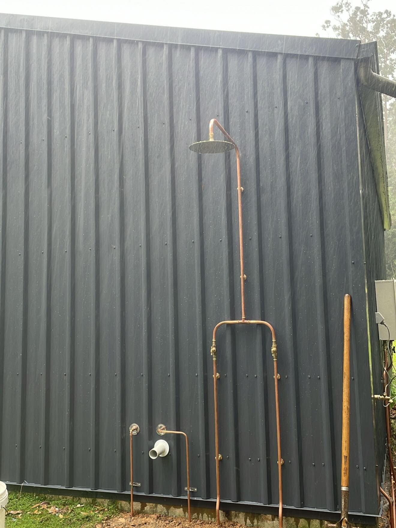 Exposed copper outdoor shower against dark corrugated cladding