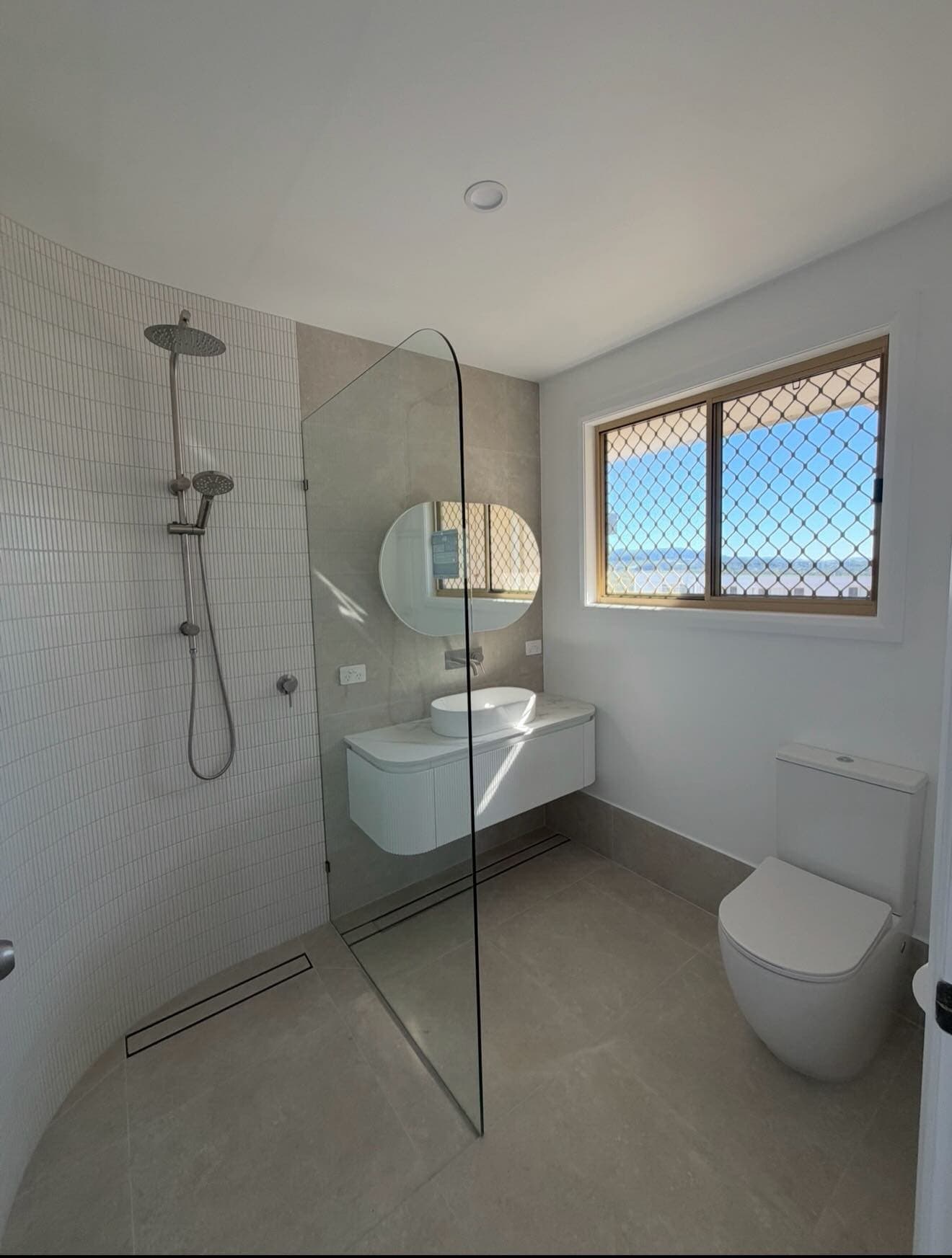 Curved-wall ensuite with a frameless glass shower screen and a vessel basin