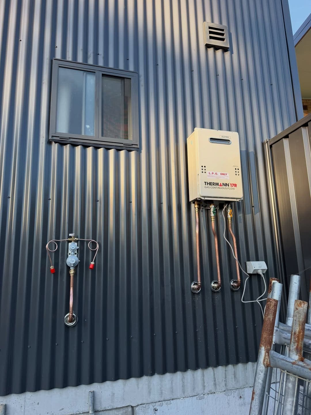 Continuous-flow gas hot water unit mounted on a commercial shed wall